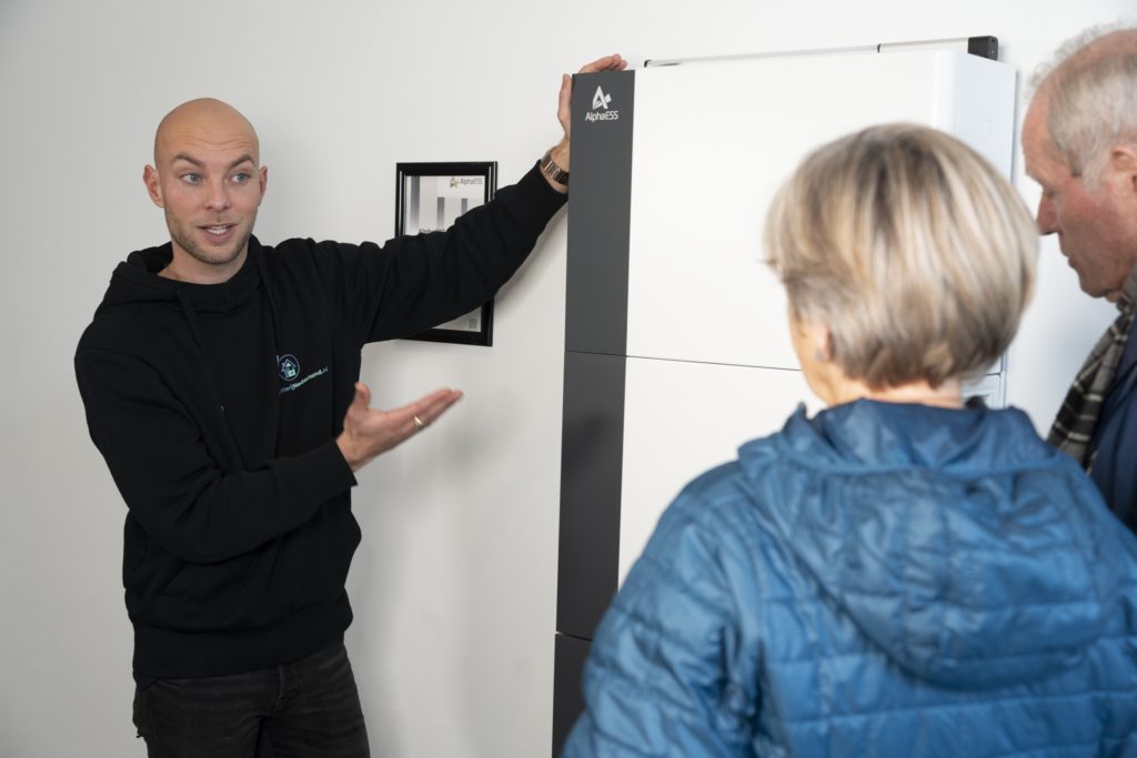 Adviseur van ThuisbatterijNederland legt een thuisbatterij uit aan twee klanten in de showroom