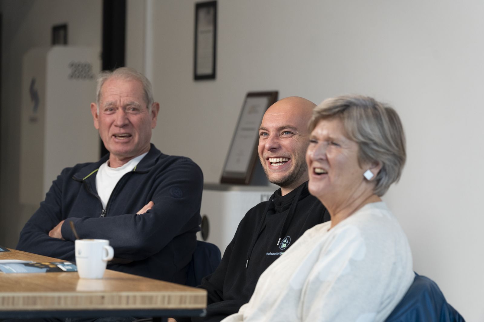Tevreden bezoekers lachen samen met de adviseur aan tafel in de showroom